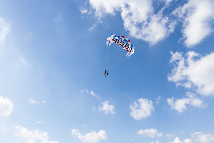 Person parasailing under a colorful parachute against a blue sky with clouds.
