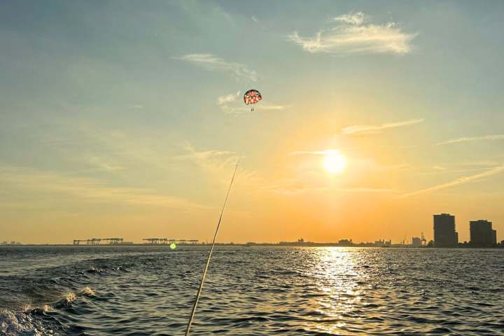 Parasailing over water at sunset with city skyline in the distance.