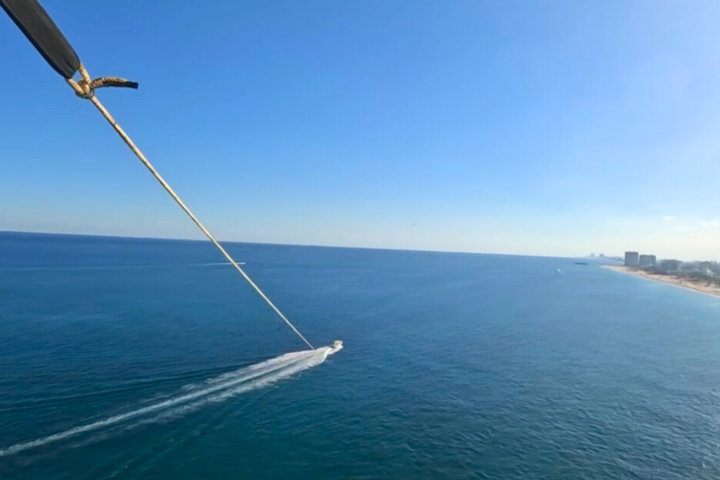 Parasailing view over ocean with boat below and city skyline in distance.