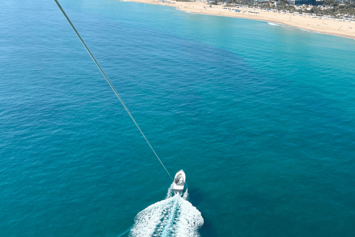 Boat in clear blue water pulling a parasail near a sandy beach.