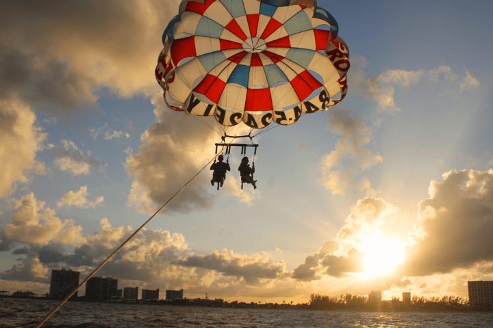 Two people parasailing over ocean with colorful parachute at sunset.
