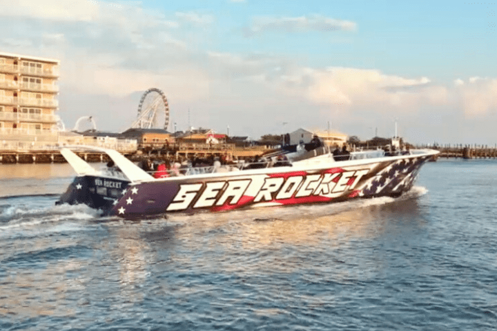 Speedboat named 'Sea Rocket' cruising near a pier with a ferris wheel and buildings in the background.
