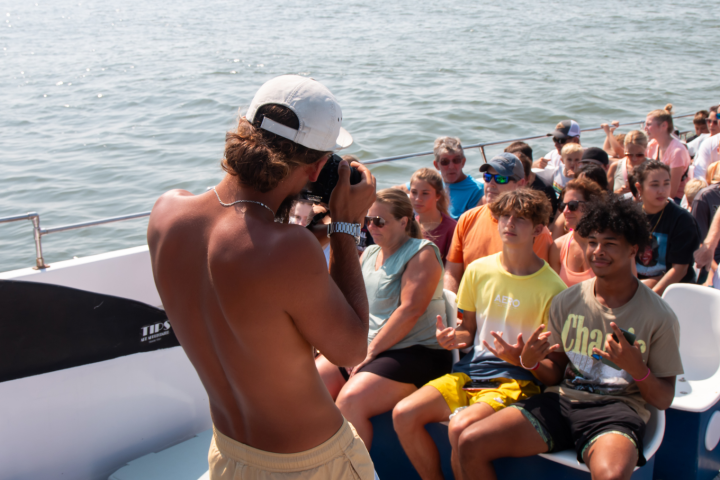 Group of people on a boat, one person taking photos, others seated and smiling.