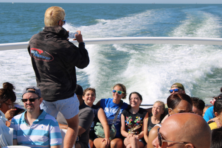People seated on a boat, one person standing and taking photos.