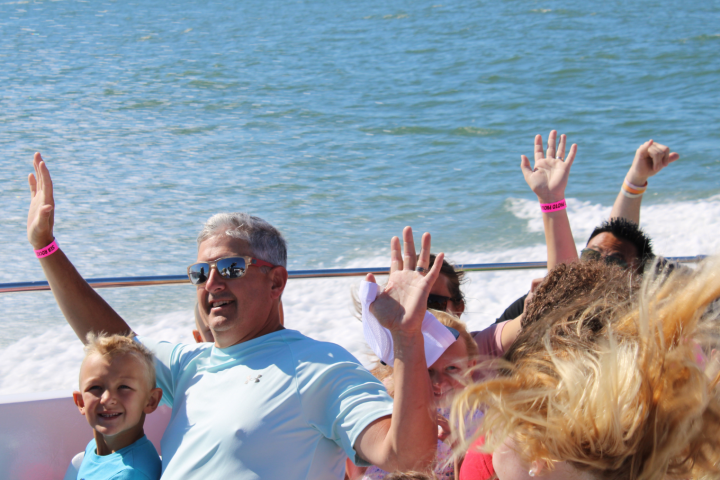 People on a boat raising hands, enjoying a sunny day on the water.