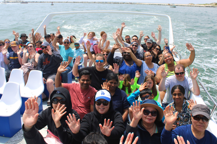 Group of people waving on a boat with ocean in the background.