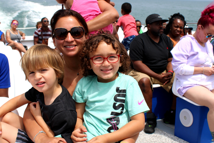 Woman and two children smile while seated on a boat with other passengers.