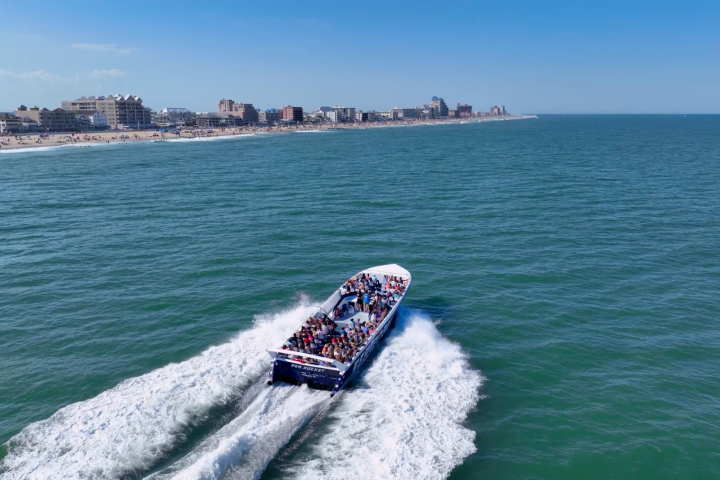 Speedboat with passengers cruising along a coastline on a sunny day.