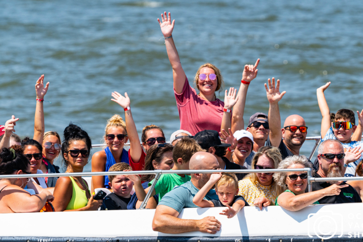 Group of people on a boat waving and smiling on a sunny day.