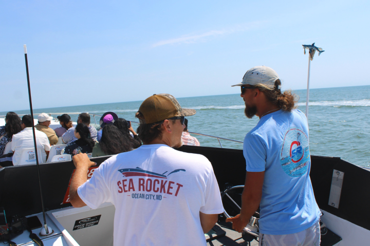 People on a boat ride, with two crew members steering, under a clear blue sky.