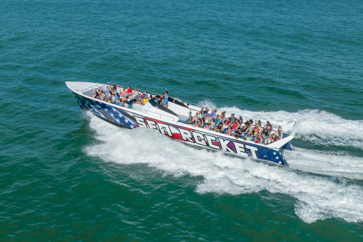Speedboat with passengers on blue ocean water, creating waves.