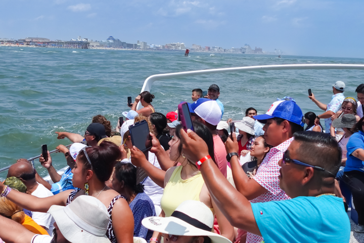 People on a boat taking photos of the ocean and distant shoreline.