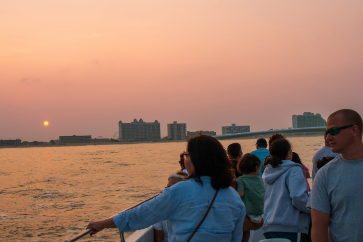 People on a boat at sunset with city skyline in background.