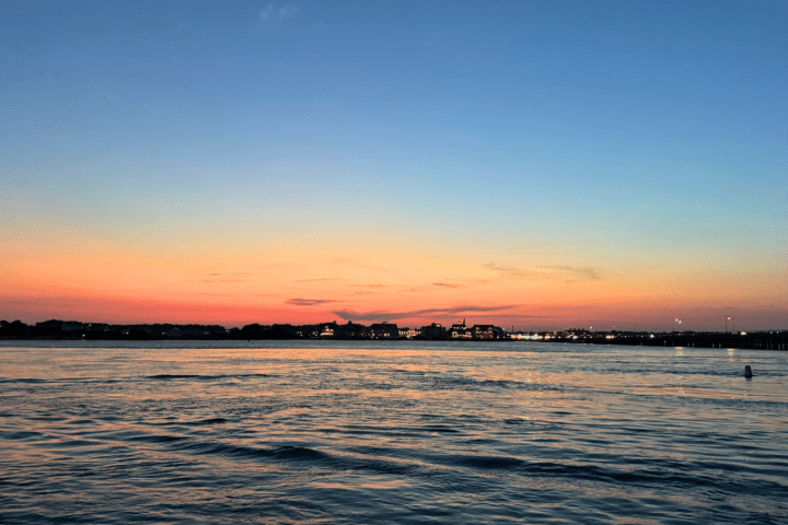 Calm water at sunset with colorful sky and distant shoreline.