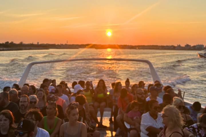 Group of people on a boat at sunset, with a clear sky and calm water.