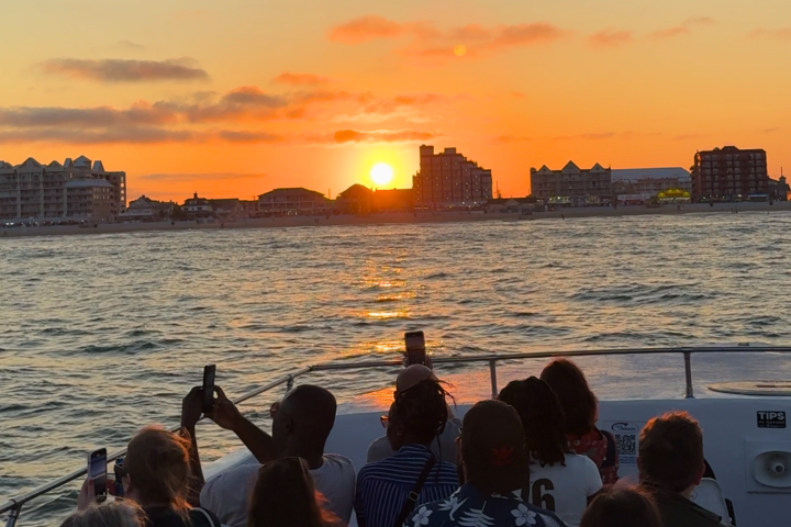 People on a boat watching a sunset over city buildings.