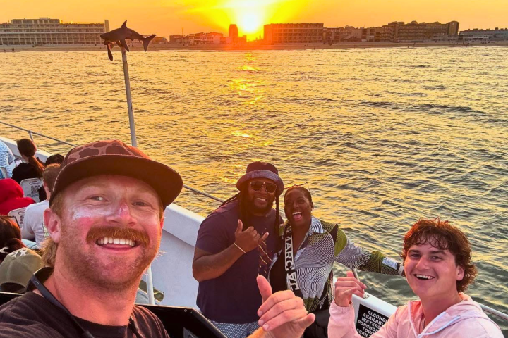 Group of people on a boat at sunset, posing and smiling.