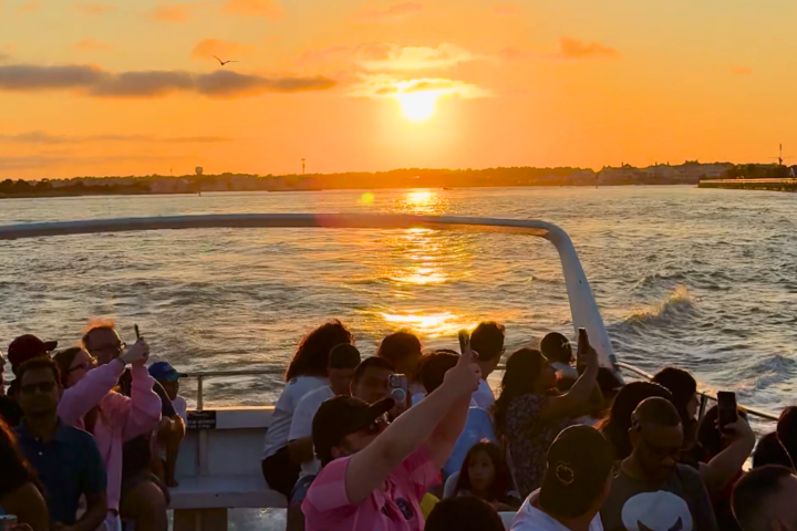 People enjoy sunset on a boat with the sun reflecting on the water.