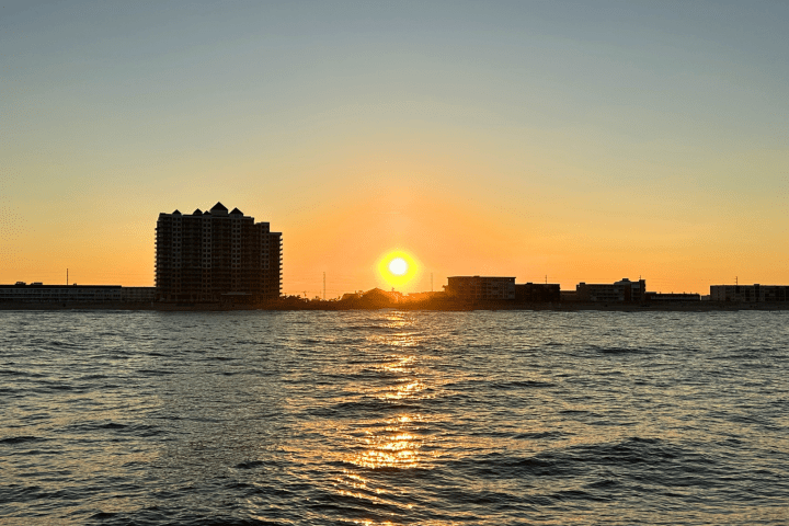 Sunset over water with buildings silhouetted against the sky.