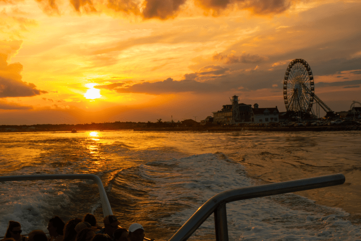 Sunset over ocean with ferris wheel in distance and people on a boat.