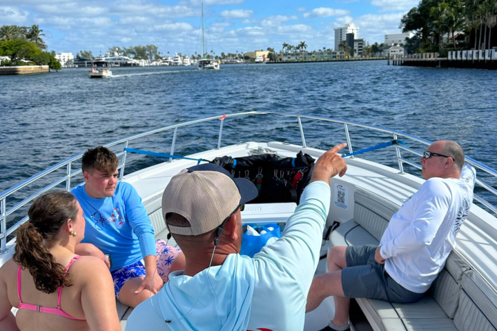 Four people relax on a boat with cityscape and blue sky in the background.