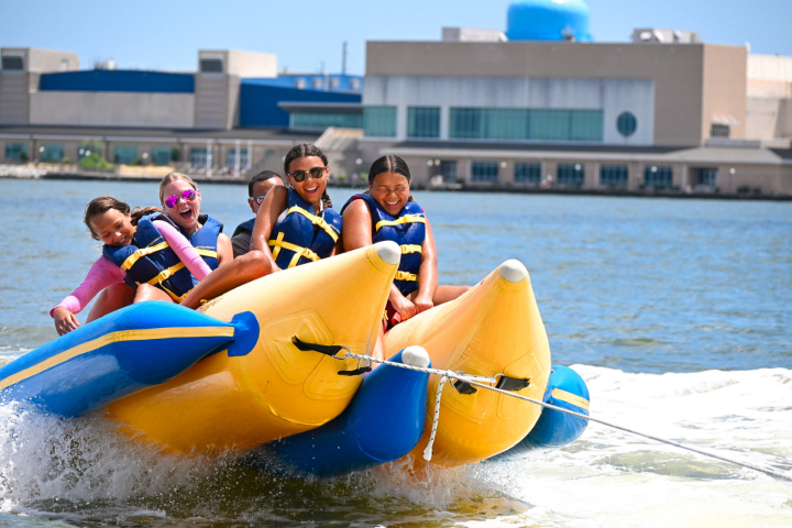 Five people on an inflatable banana boat being towed on water.