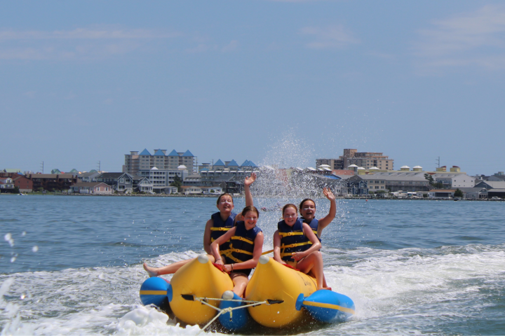 Group of people on an inflatable banana boat in the ocean near buildings.