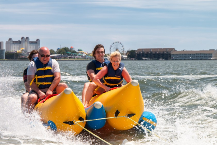 Group riding a banana boat on the water near a city skyline.