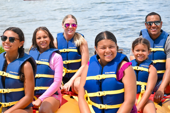 Group of people in life jackets sitting on an inflatable raft on a lake.