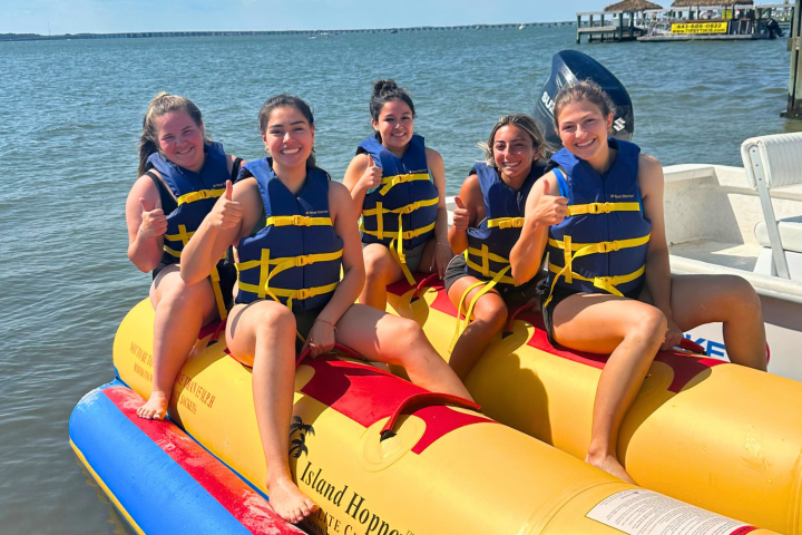 Five people in life jackets giving thumbs up on inflatable banana boat.