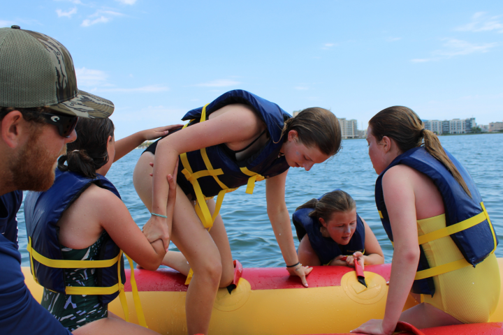 People in life jackets climbing onto a banana boat on water.