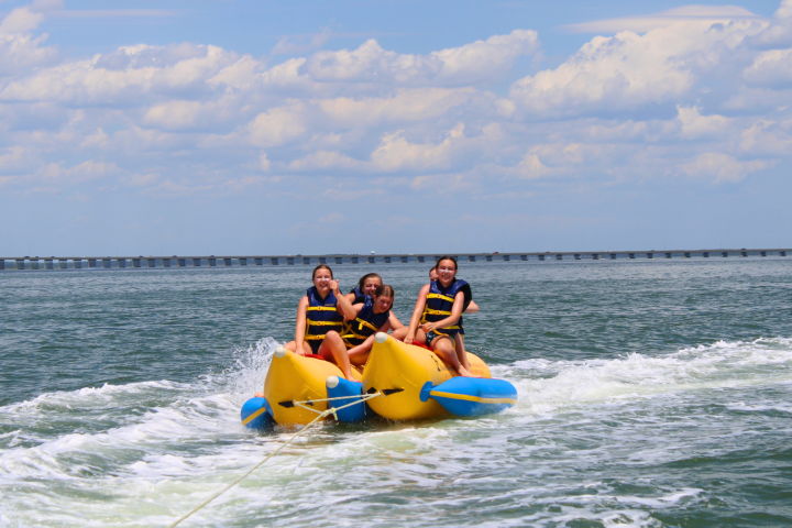 Four people riding a banana boat on the water under a cloudy sky.