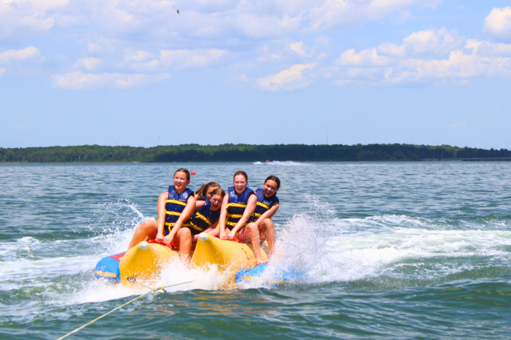 Four people riding an inflatable banana boat on a lake.