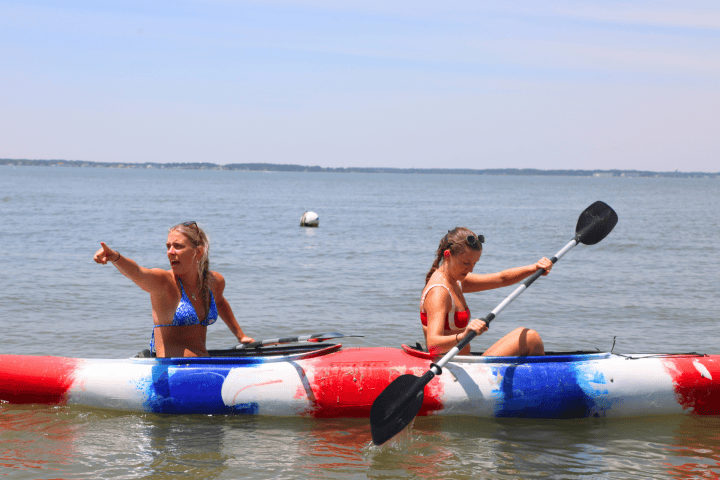 Two people in a kayak on a calm lake, one pointing, the other paddling.