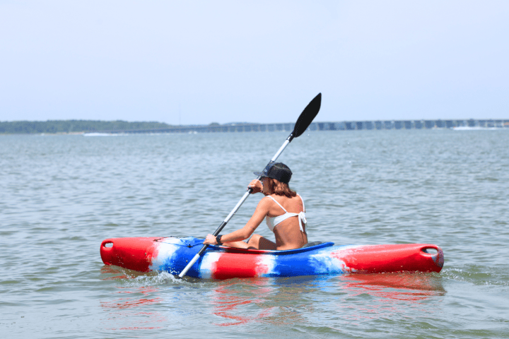 Person in a red, white, and blue kayak paddling on calm water.