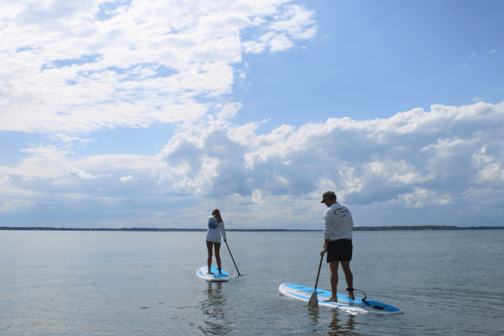 Two people paddleboarding on a calm lake under a partly cloudy sky.