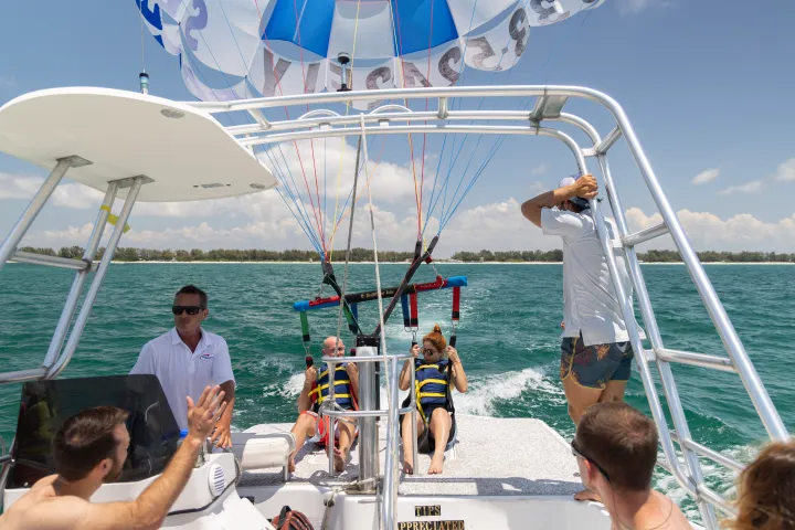 People on a boat preparing for parasailing over the ocean with a parachute visible overhead.
