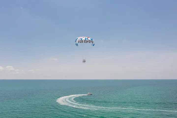 Parasailing over ocean with a boat creating wake on a sunny day.