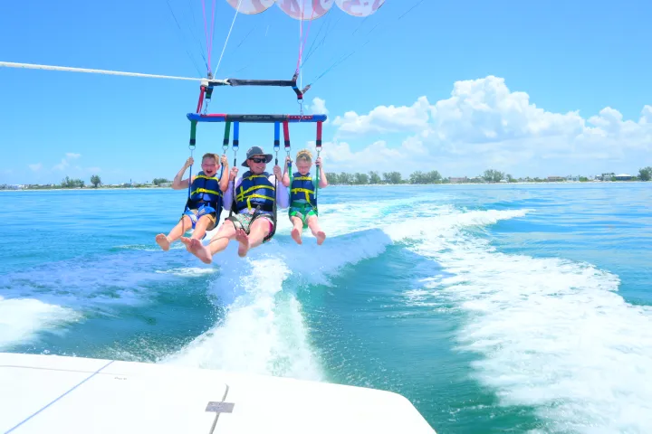 Three people parasailing over water with a clear blue sky and distant shoreline.