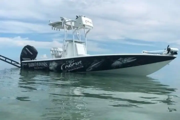 A white fishing boat with logos floats on calm water under a cloudy sky.