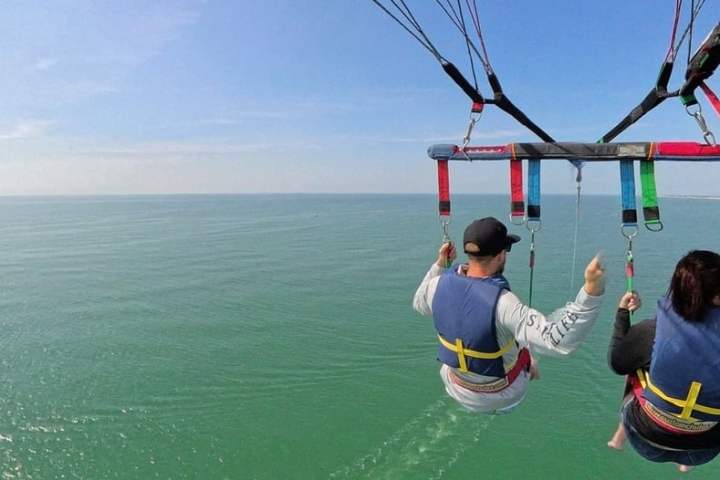 Two people parasailing over a calm ocean with clear skies.