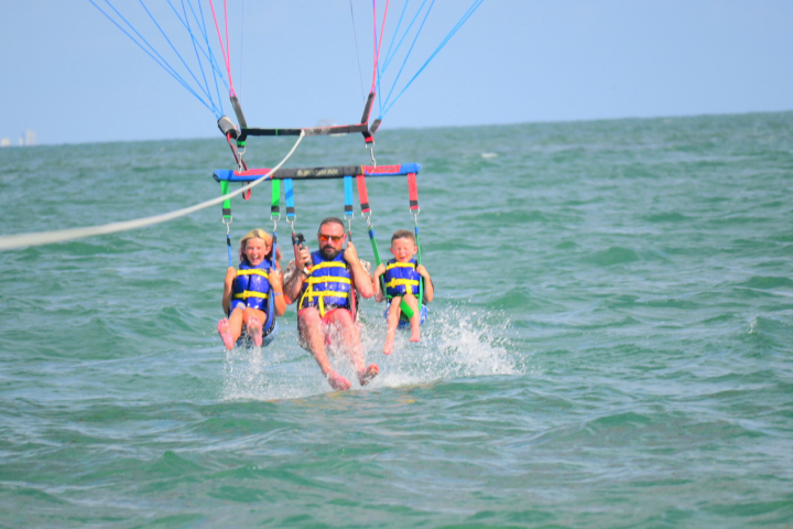 Three people parasailing over water, wearing yellow and blue safety harnesses.