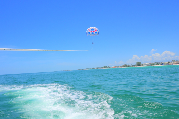 Parasailer over the ocean with clear blue sky and distant shoreline.