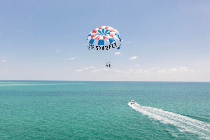 Two people parasailing over turquoise ocean, action boat below, clear sky.