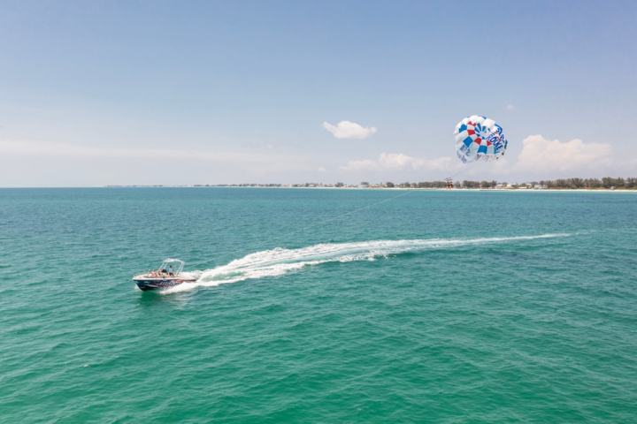 Boat towing a parasailer over turquoise sea, under a clear sky.