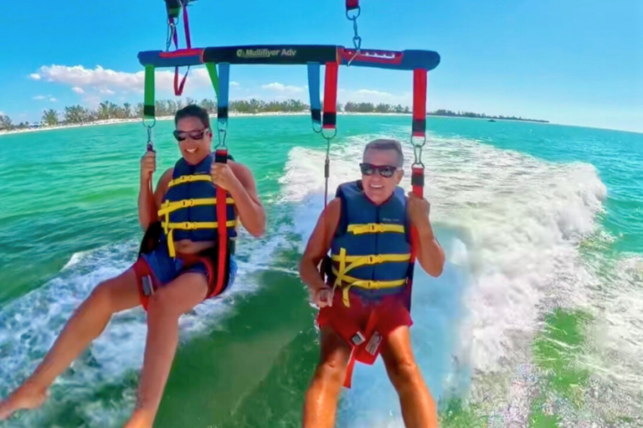 Two people parasailing above turquoise ocean water with clear sky.