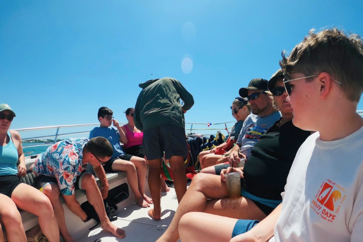 Group of people in casual wear sitting on a boat under a clear blue sky.