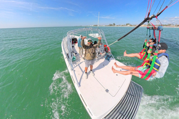People parasailing over water, launched from a boat with crew assisting.
