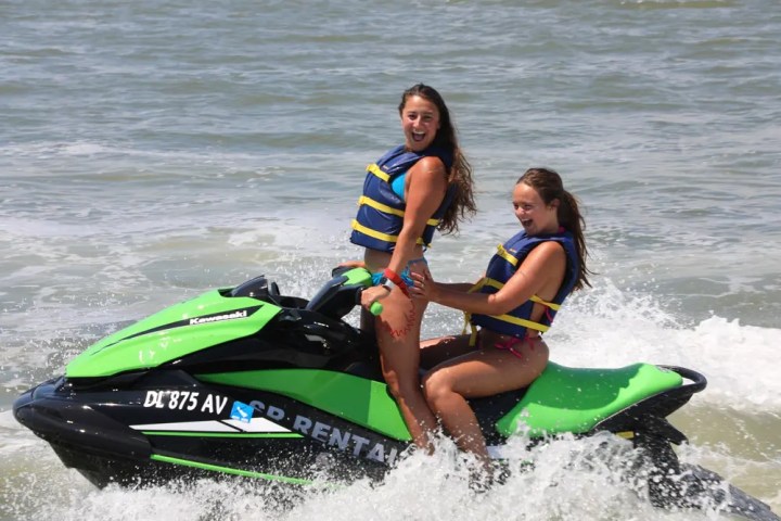 Two people on a green jet ski wearing life vests, riding on the water.