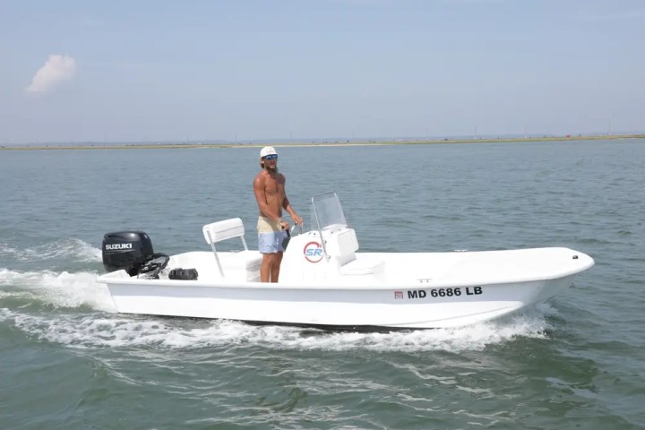Man steering a small white motorboat on open water.